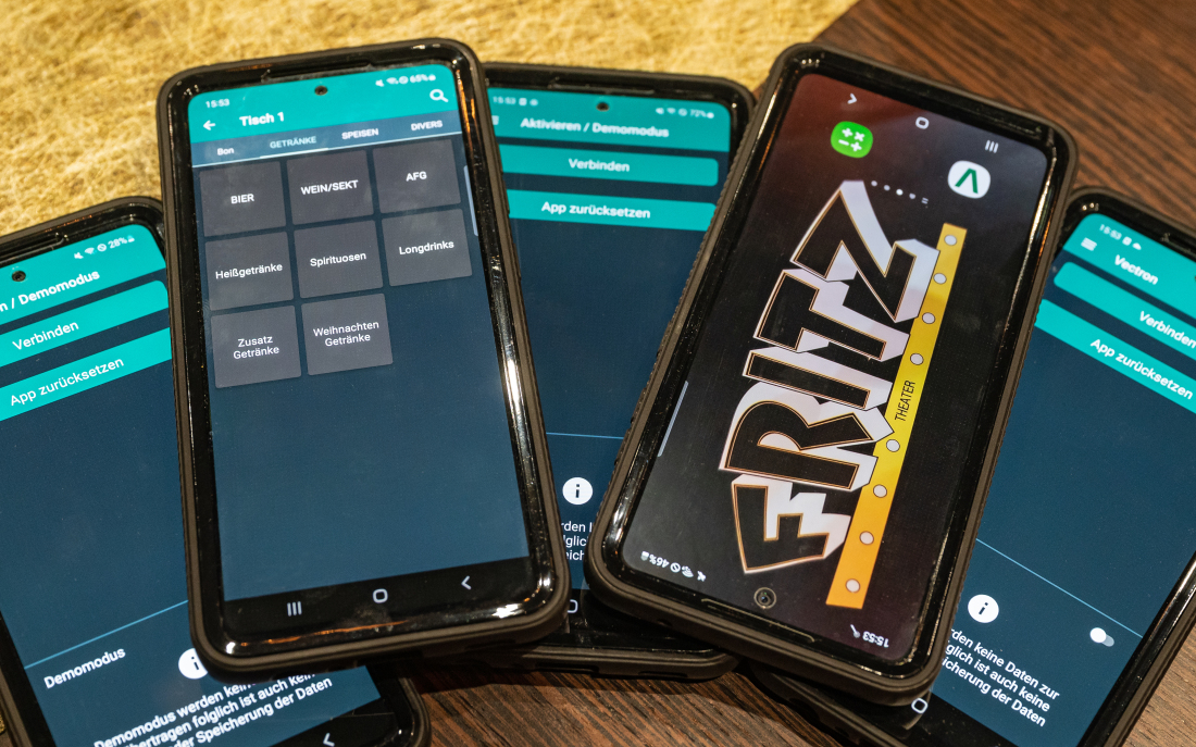 Fünf Mobiltelefone liegen auf einem Tisch, auf einem ist das Loto des FRITZ Theaters, auf den anderen verschiedene Seiten eines Buchungssystems für Gastronomie und Veranstaltungen.