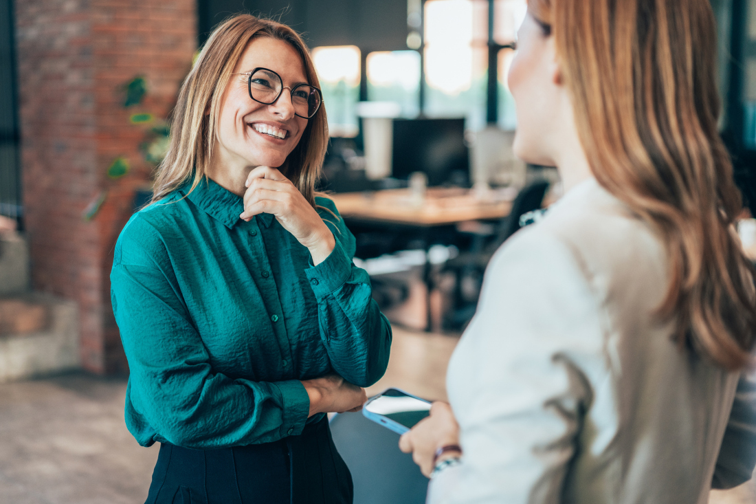 Zwei Frauen in Business-Kleidung sind in ein Gespräch vertieft.