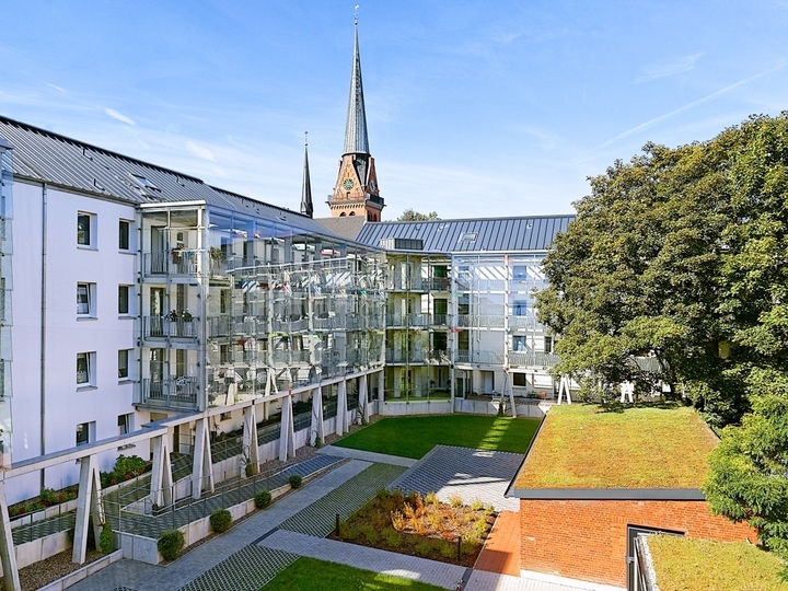 Ein Mehrparteienhaus nach der Renovierung von außen mit weißer Fassade und neuen Balkonen